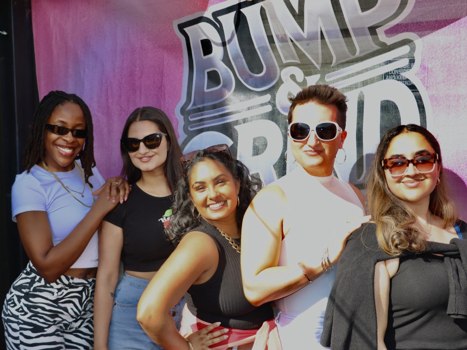 Five friends posing together in front of the Bump & Grind photo backdrop